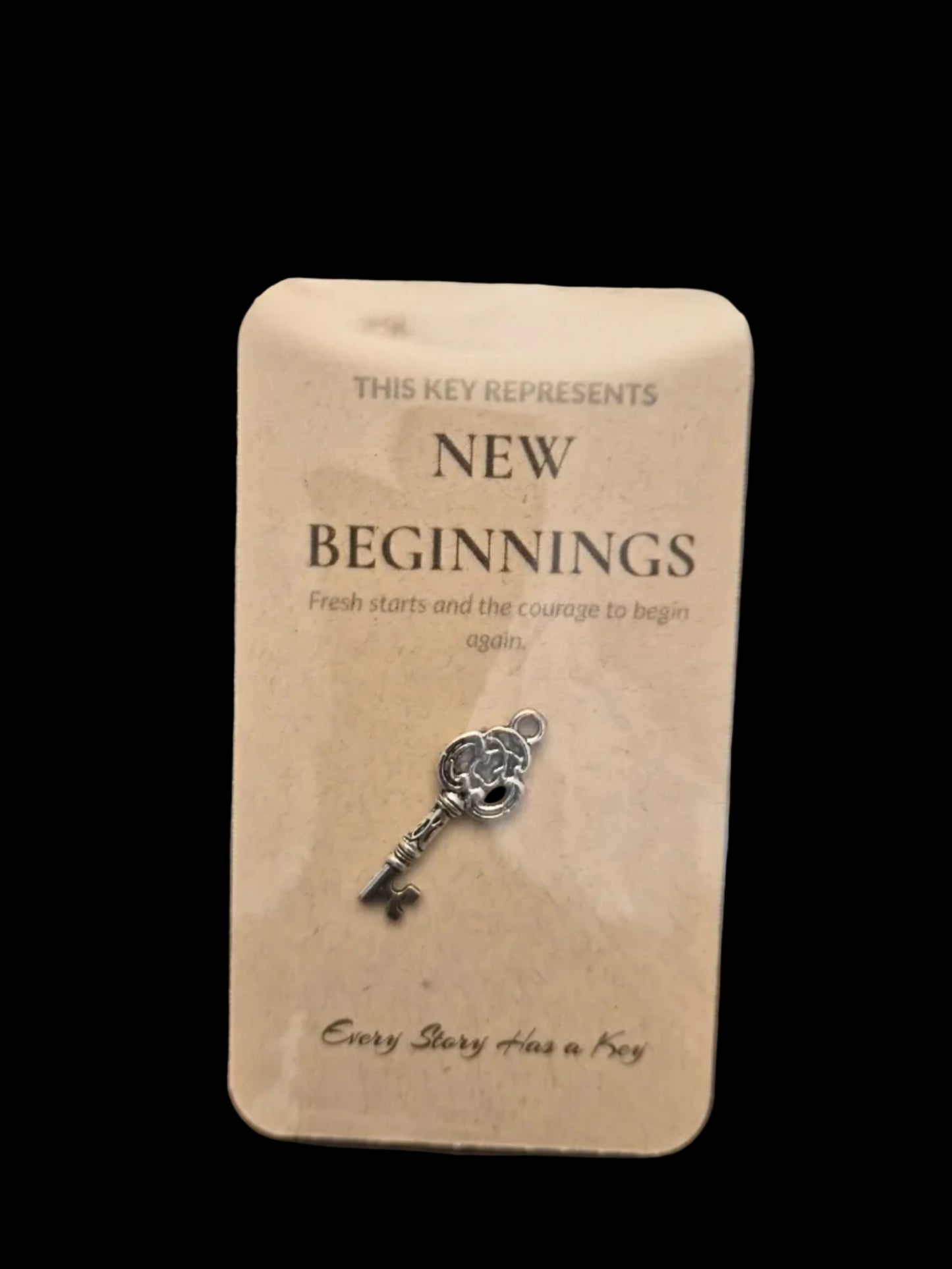Key-shaped pendant on a card with 'New Beginnings' text, held in clear plastic packaging.
